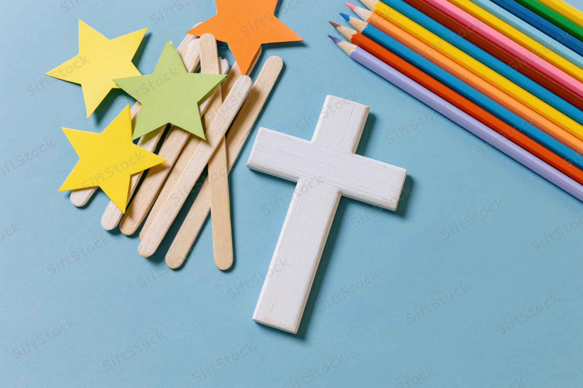 White wooden christian cross with craft sticks and colored pencils on blue background