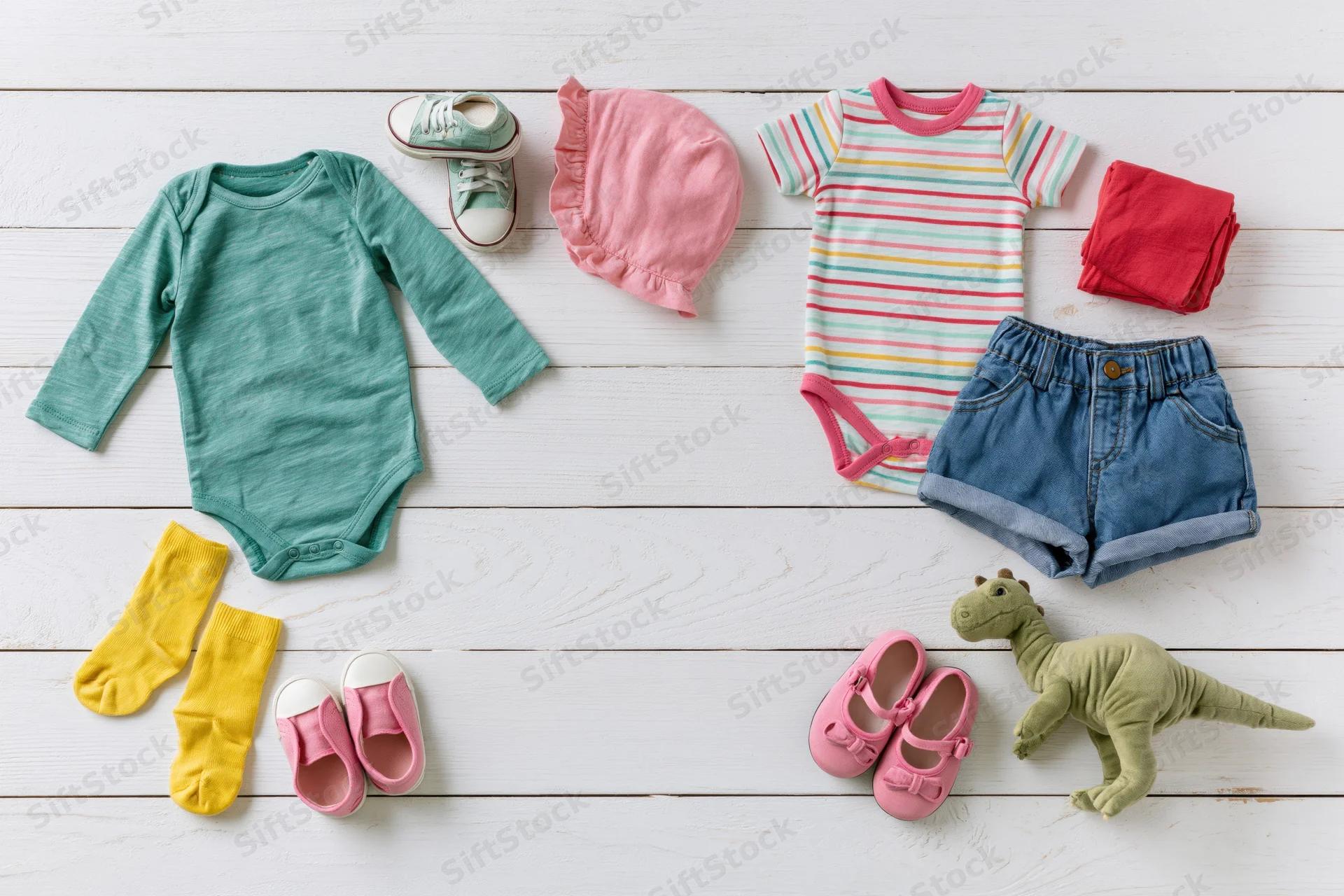 Baby clothing and accessories arranged in flat lay on white wooden floor