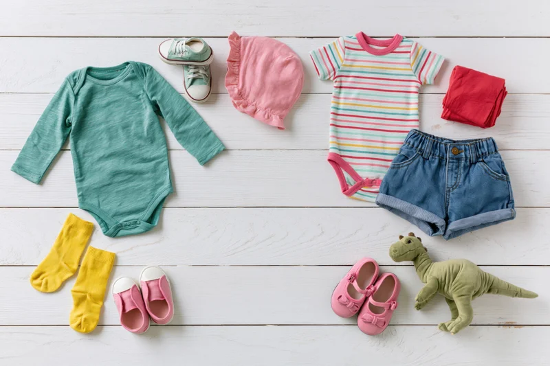 Baby clothing and accessories arranged in flat lay on white wooden floor