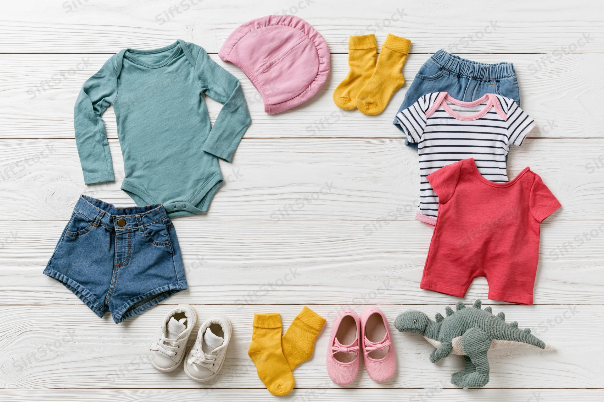 Baby clothing and accessories arranged in a circle on a white wooden floor