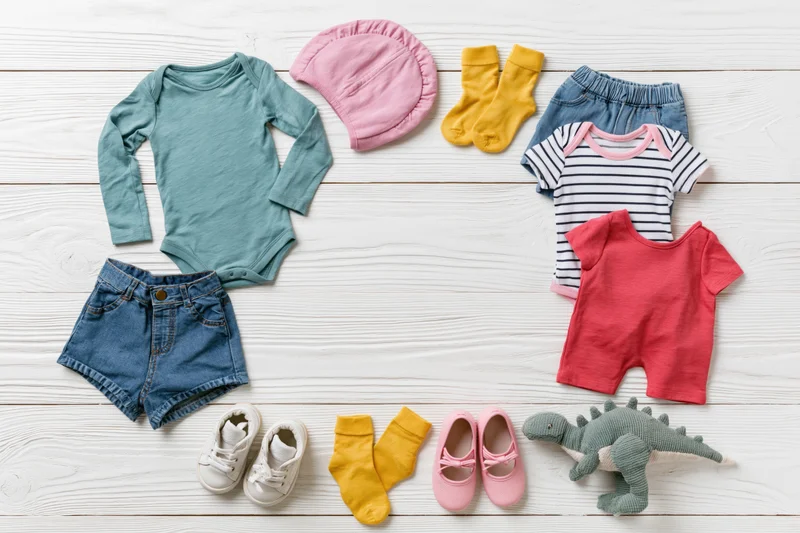 Baby clothing and accessories arranged in a circle on a white wooden floor