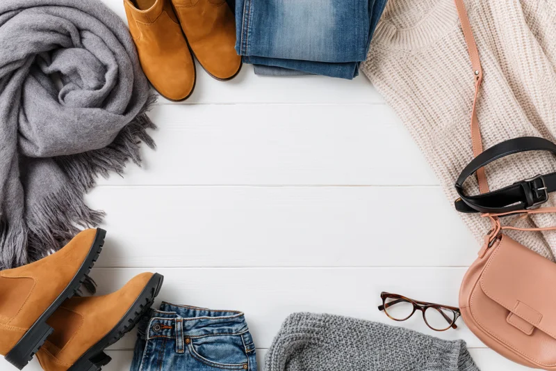 Autumn casual clothing and accessories arranged in a flat lay on white wooden surface with copyspace
