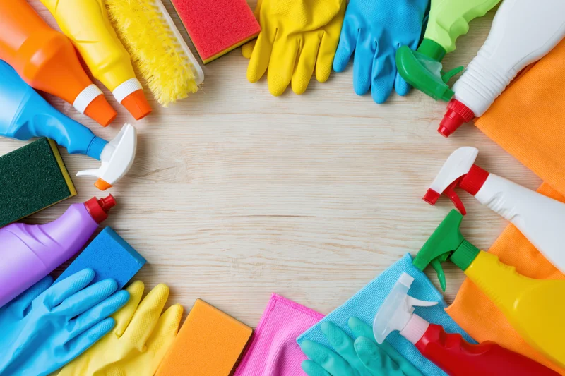 Colorful cleaning supplies arranged in a circle on wooden surface with central copyspace