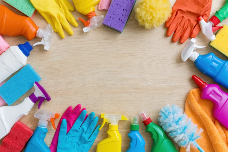 Colorful cleaning supplies arranged in a circle on wooden surface with central copyspace