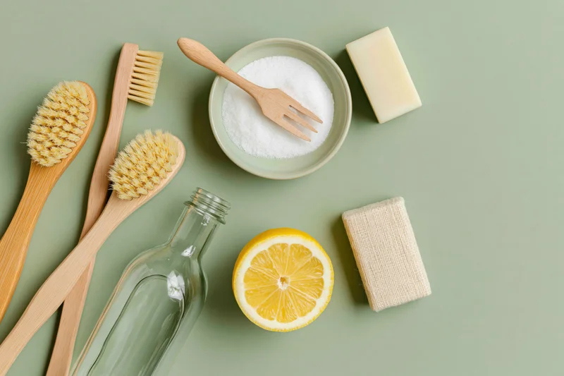 Eco-friendly cleaning supplies arranged on a muted green surface in flat lay style
