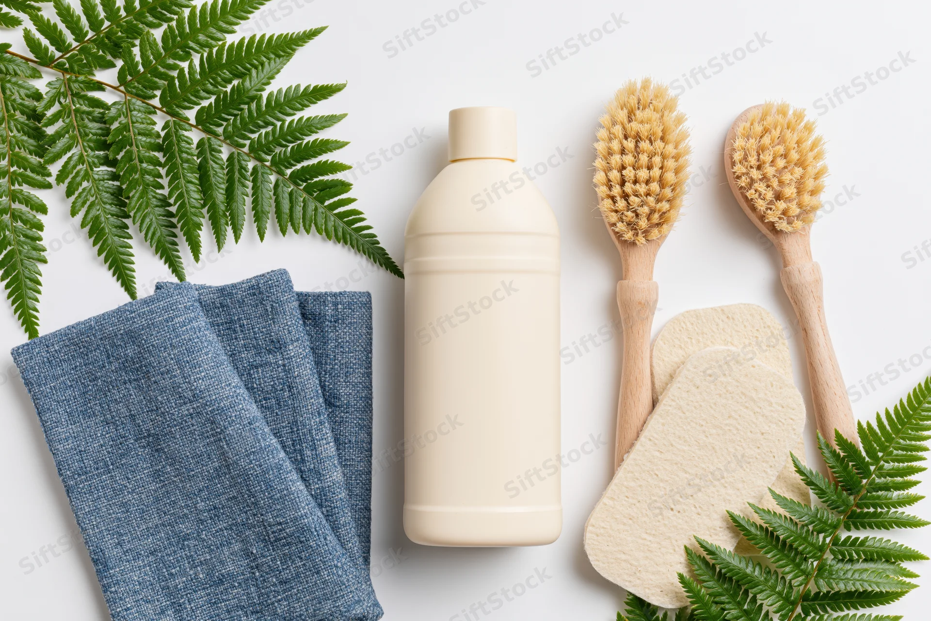 Eco-friendly cleaning supplies arranged in flat lay on white surface with fern leaves and cloth