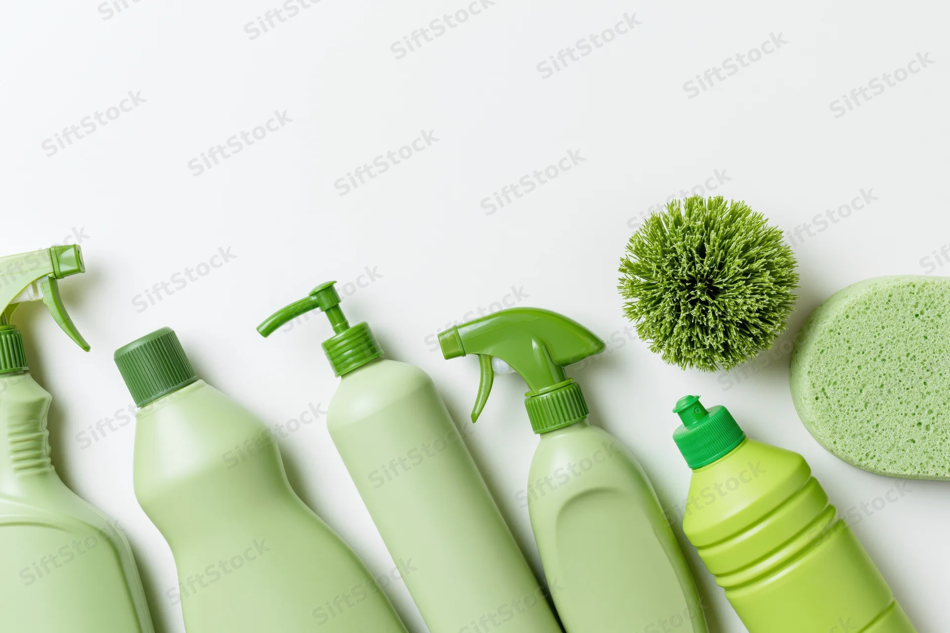 Green cleaning bottles and sponges arranged in a flat lay on white background