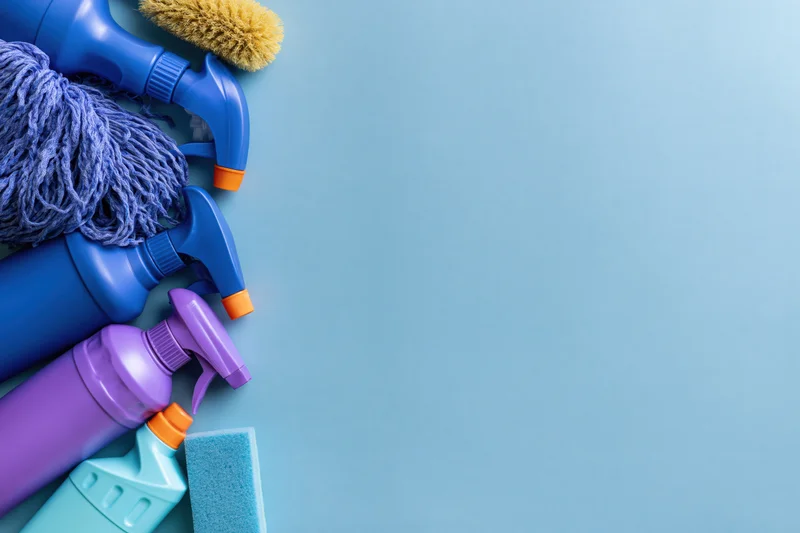 Cleaning supplies arranged along the left side of a blue surface with copyspace
