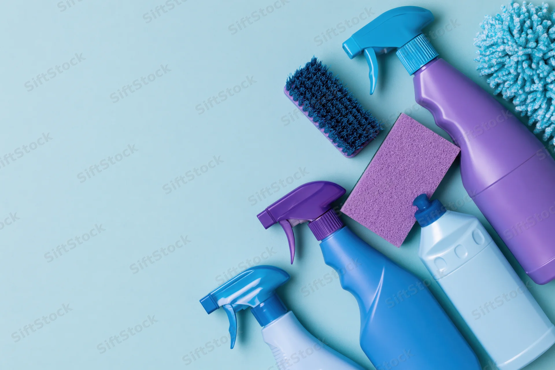Household cleaning supplies arranged in flat lay on light blue surface with copyspace