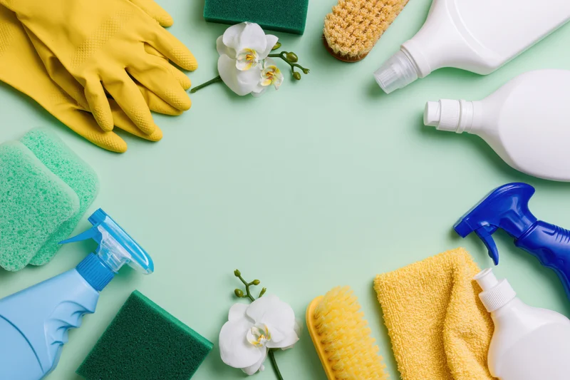 Household cleaning supplies arranged in a loose border on a mint background with copyspace
