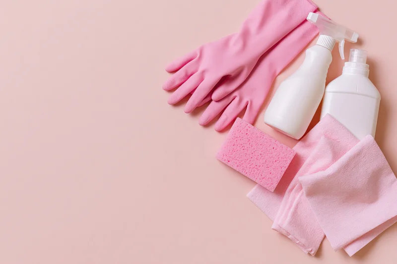 Household cleaning supplies arranged in flat lay on pink surface with copyspace