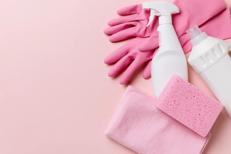 Pink cleaning supplies arranged in flat lay on pastel surface with copyspace