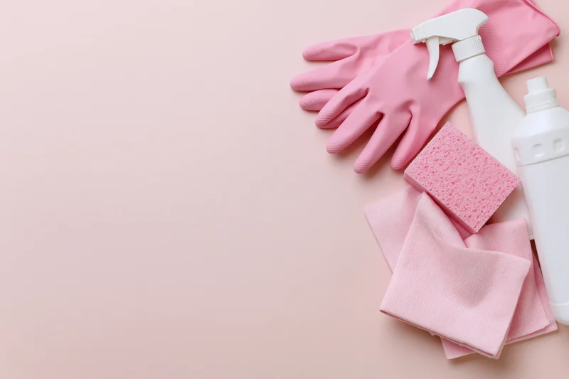 Pink cleaning supplies arranged in upper right corner on pale pink surface with copyspace