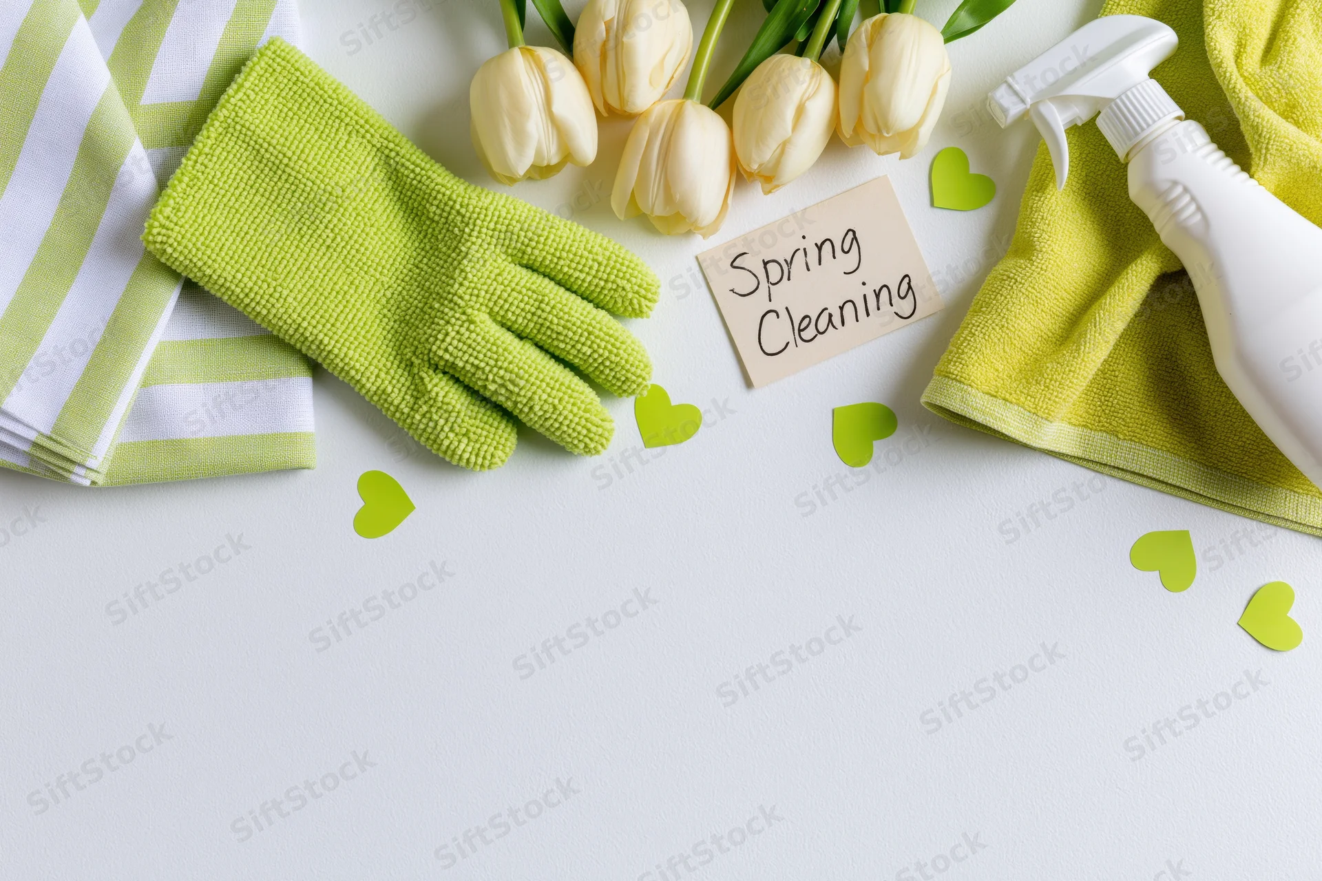 Spring cleaning supplies arranged along the top of a white surface with tulips and green hearts
