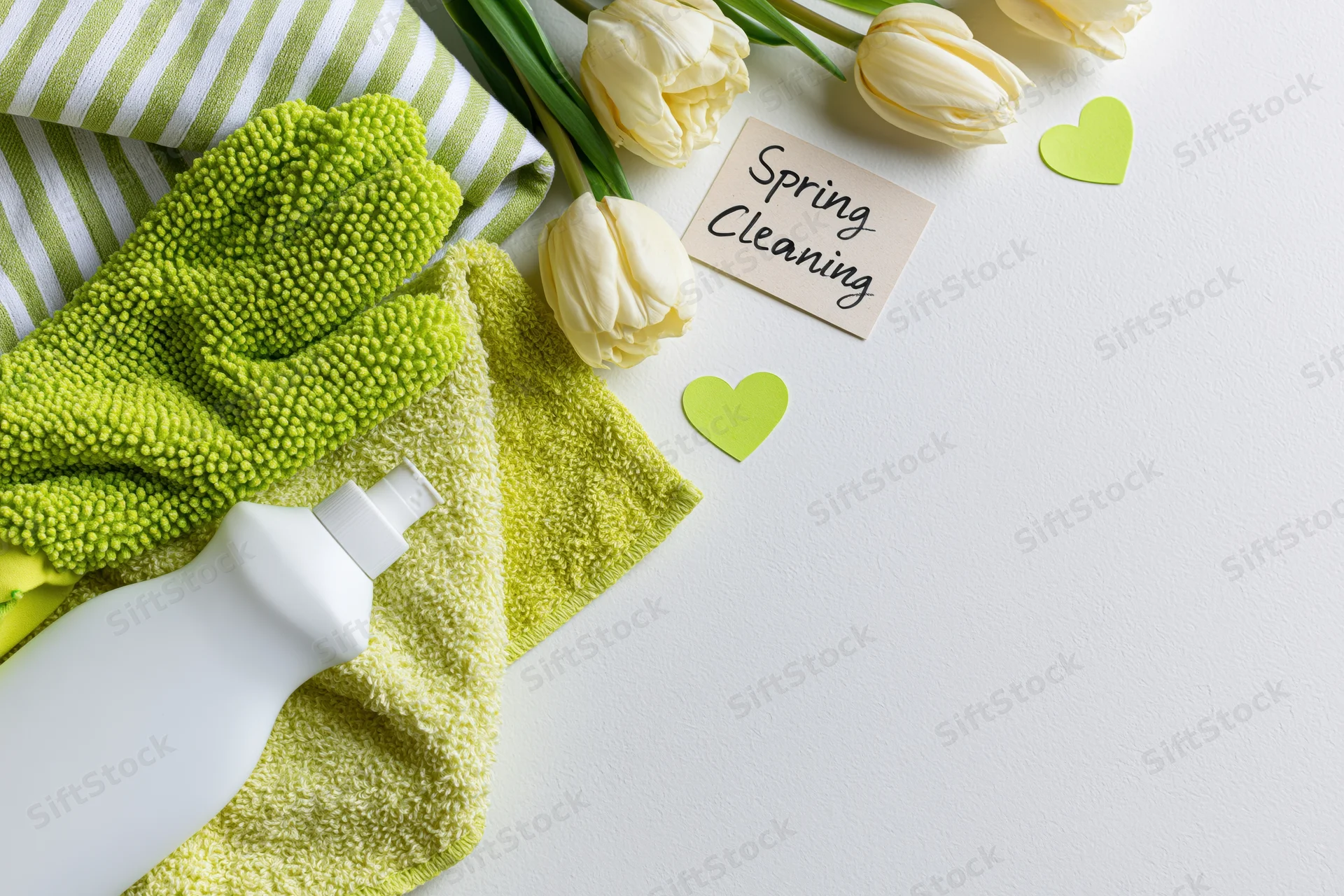 Spring cleaning supplies arranged with tulips and note on white surface