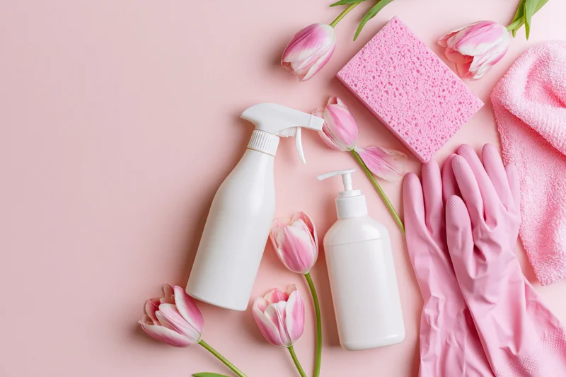Spring cleaning supplies arranged with pink tulips on pastel pink surface