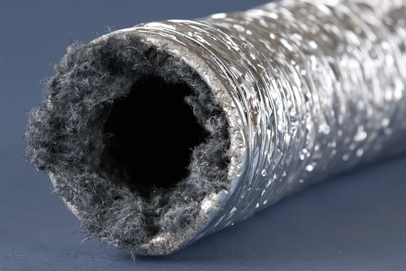 Closeup of a flexible aluminum dryer vent duct with fibrous insulation lining, lying horizontally on a dark surface