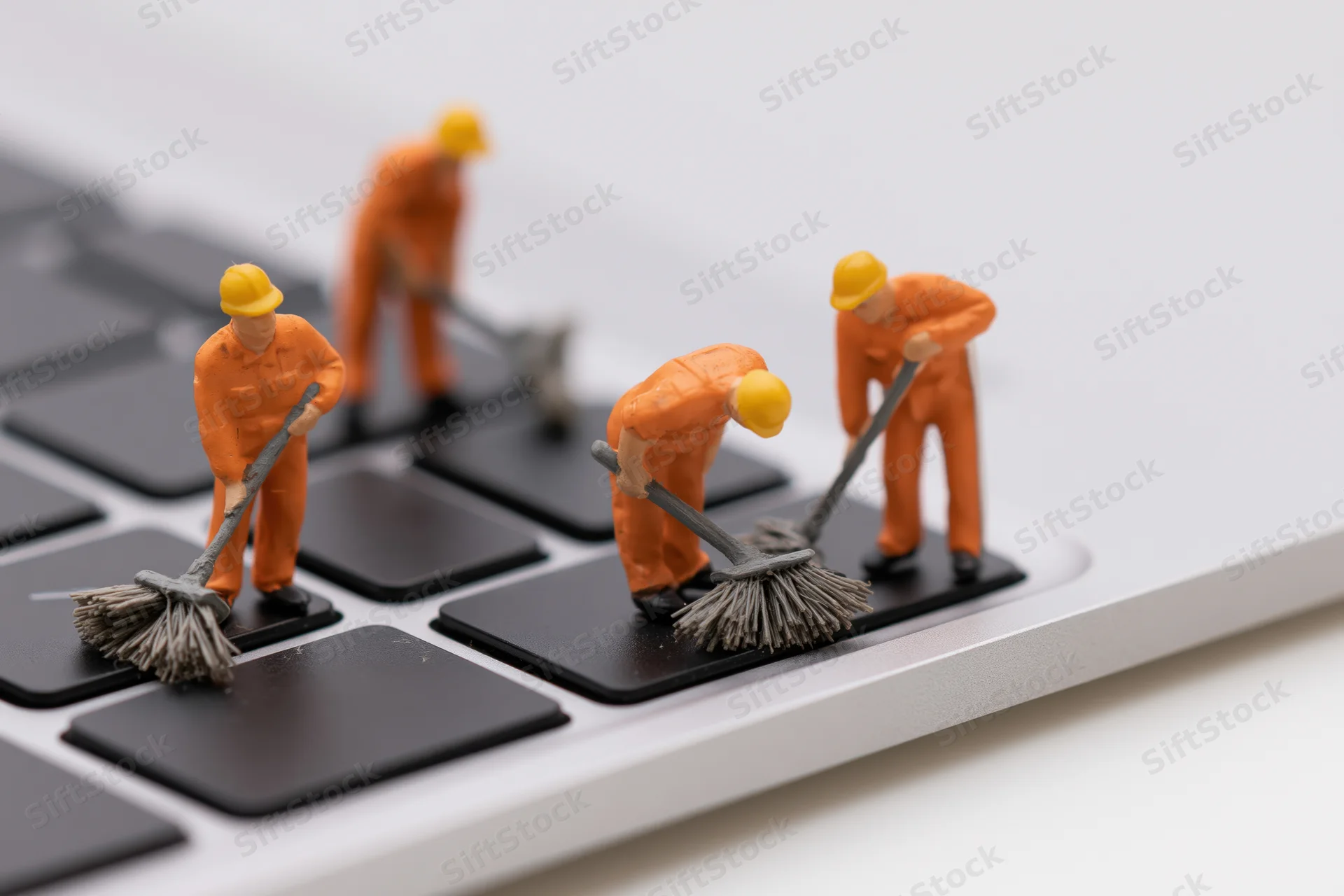 Miniature construction workers sweeping a laptop keyboard with brooms