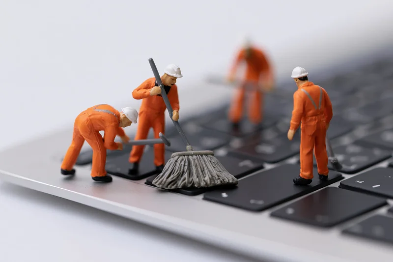 Miniature construction workers sweeping debris on a laptop keyboard