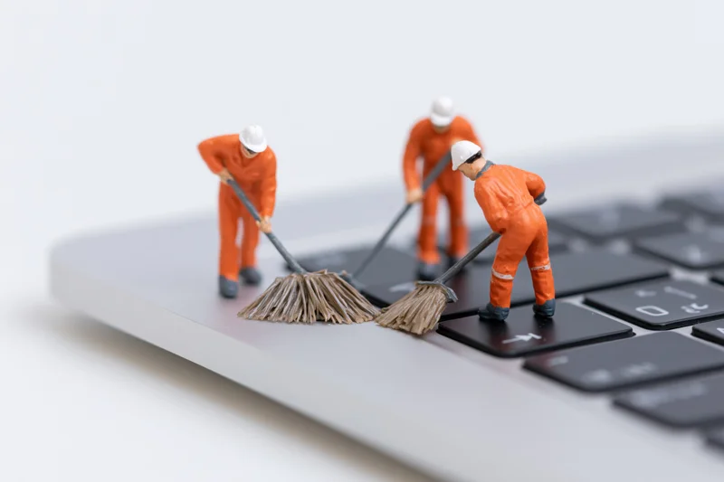 Miniature construction workers sweeping a laptop keyboard with brooms