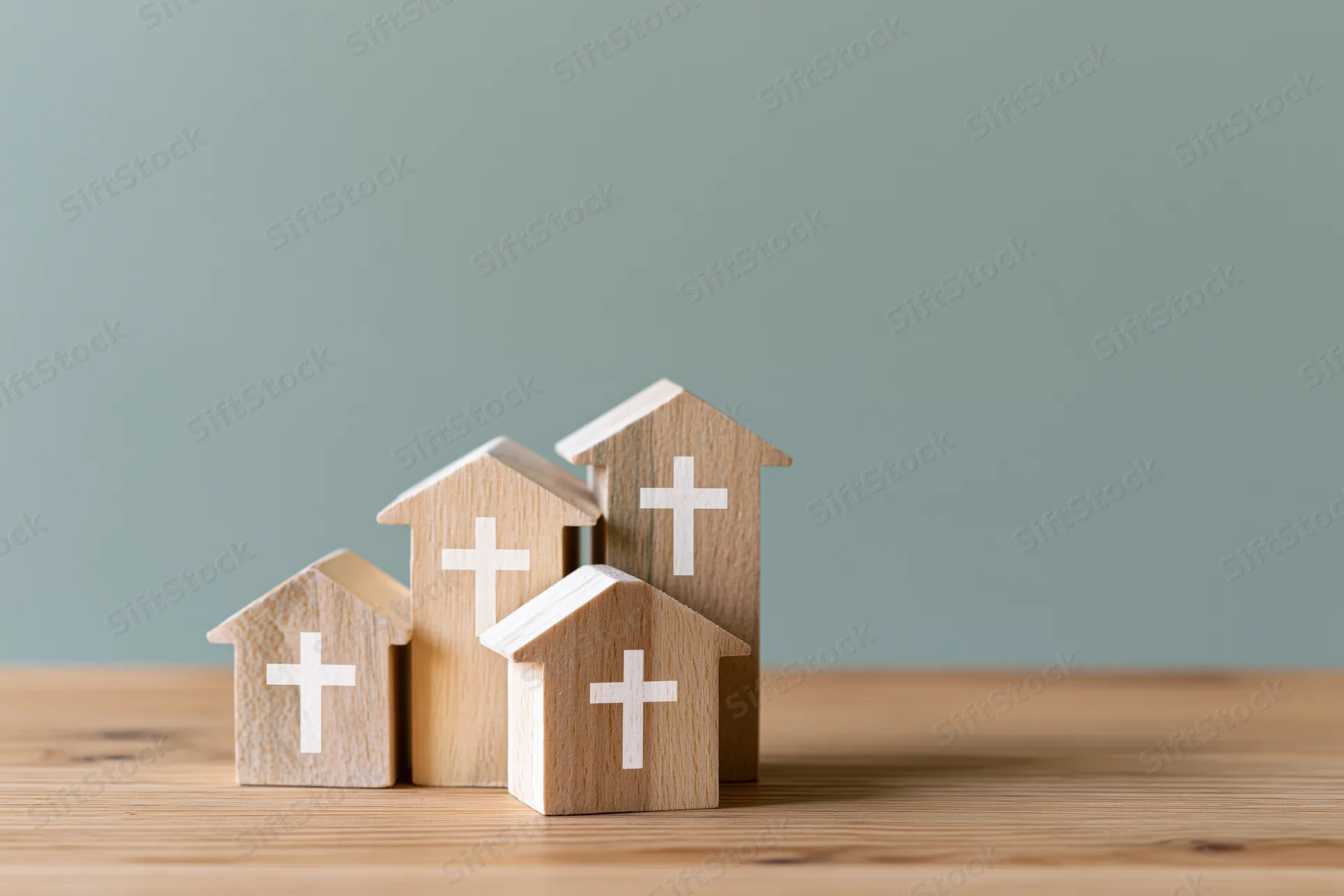 Four wooden house-shaped blocks with white crosses arranged on a wooden table