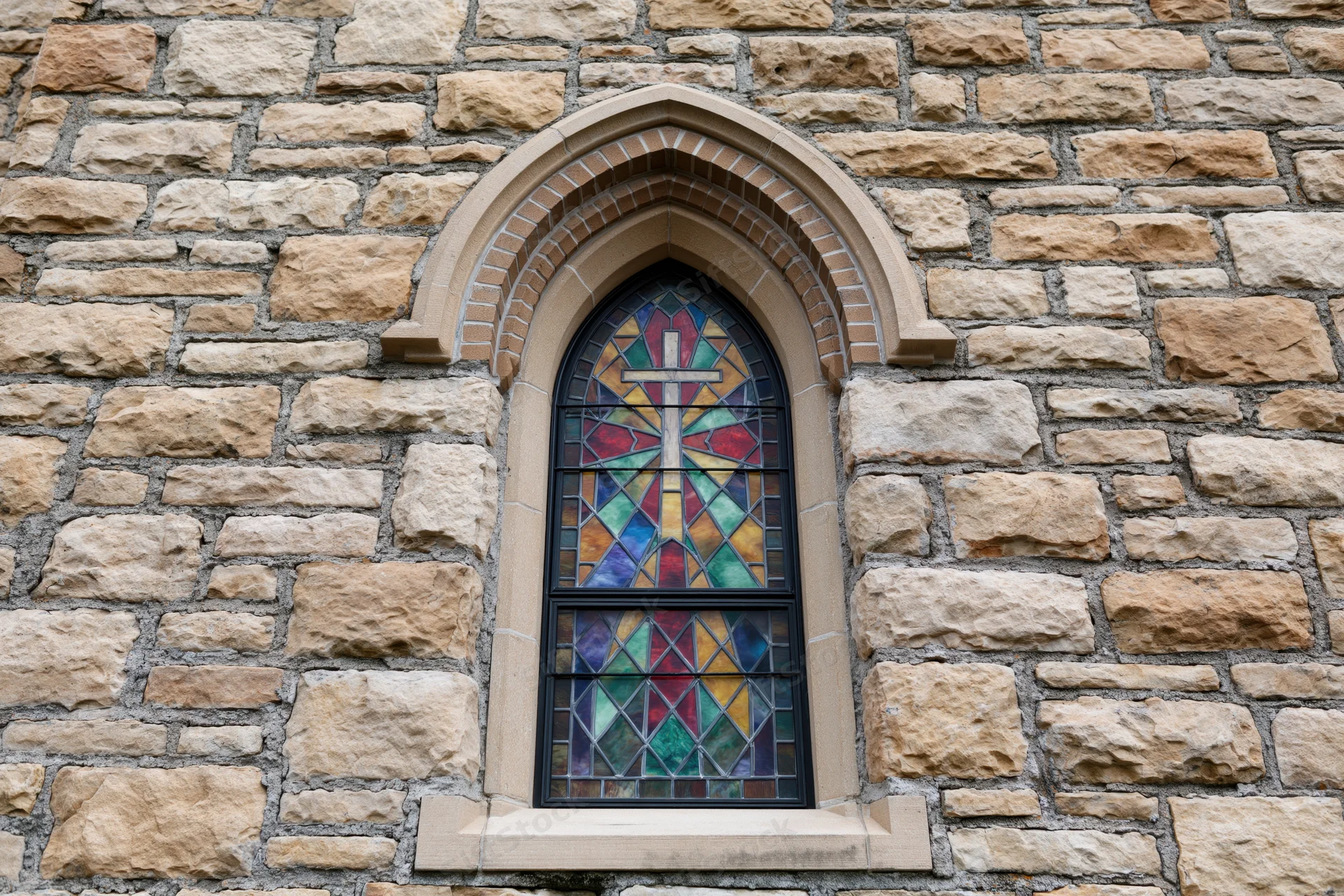 Gothic arched stained glass window with cross set in limestone church facade