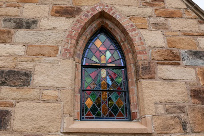 Gothic arched stained glass window set into a thick limestone facade