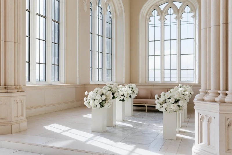 White floral arrangements on vases in a gothic chapel interior with sunlight streaming through arched windows