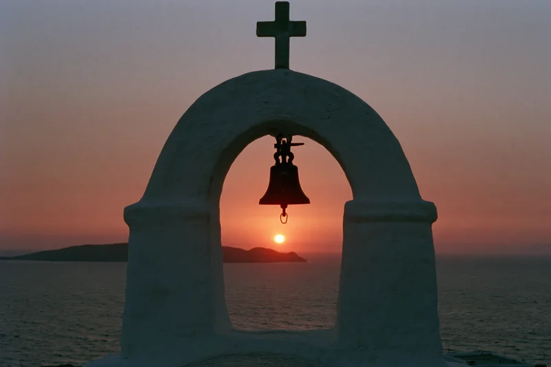 Bell tower with cross silhouetted against sunset over sea