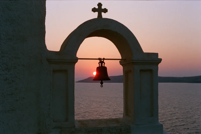 Church bell tower silhouetted against sunset over sea
