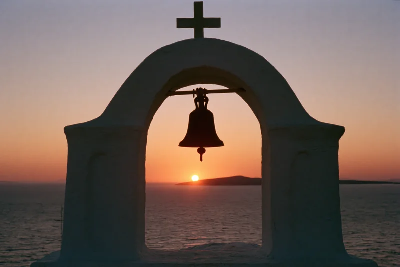 Silhouetted church bell tower with cross overlooking sea at sunset
