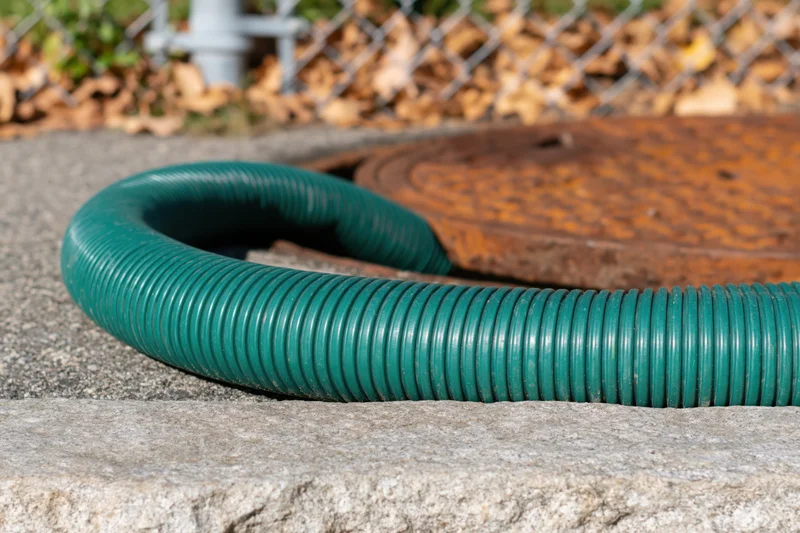 Green corrugated hose curving over concrete curb near manhole cover