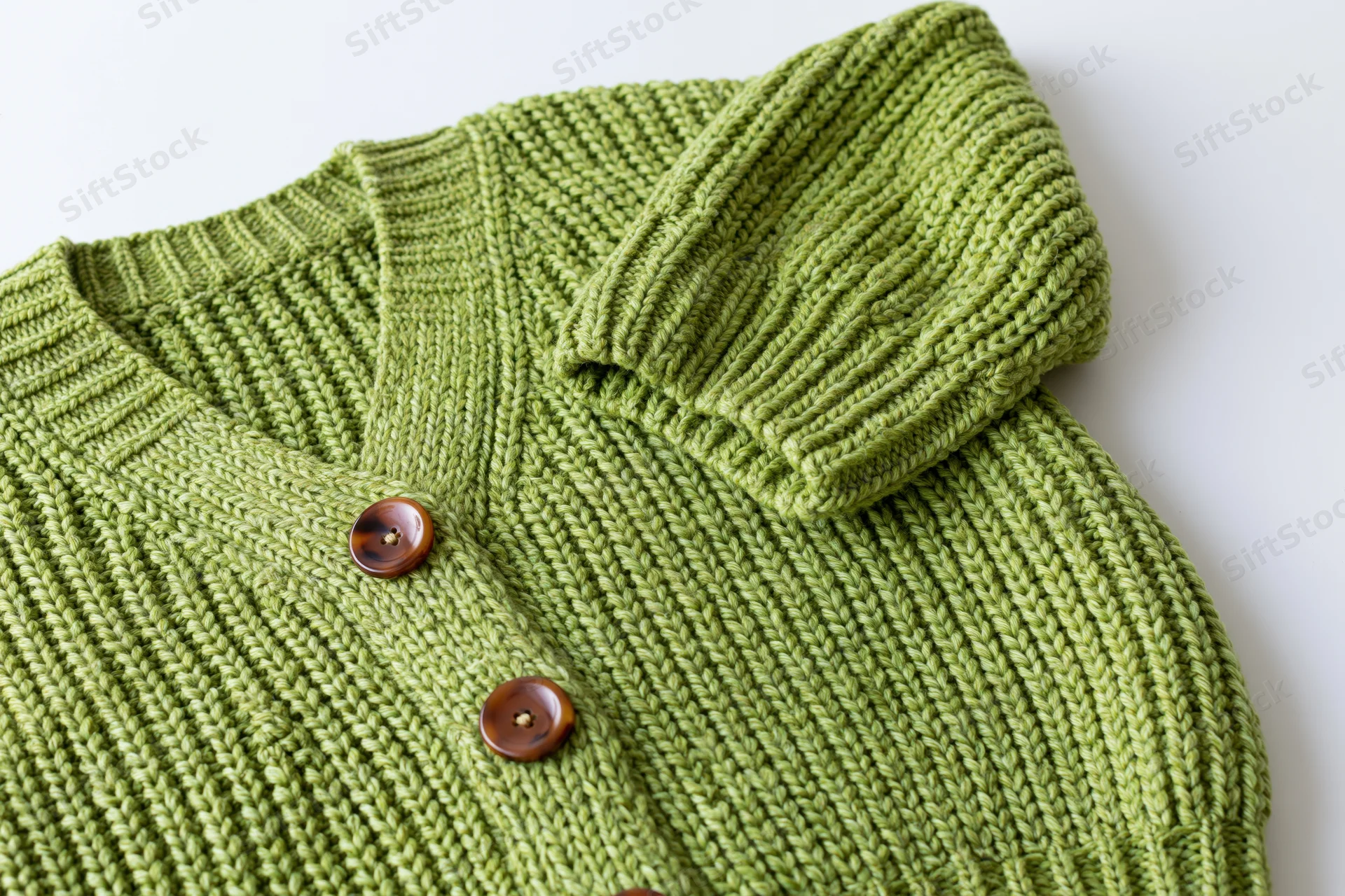 Green knit cardigan laid flat with one sleeve raised on white background