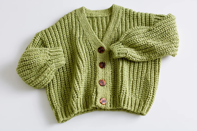 Green knit cardigan laid flat with one sleeve raised on white background