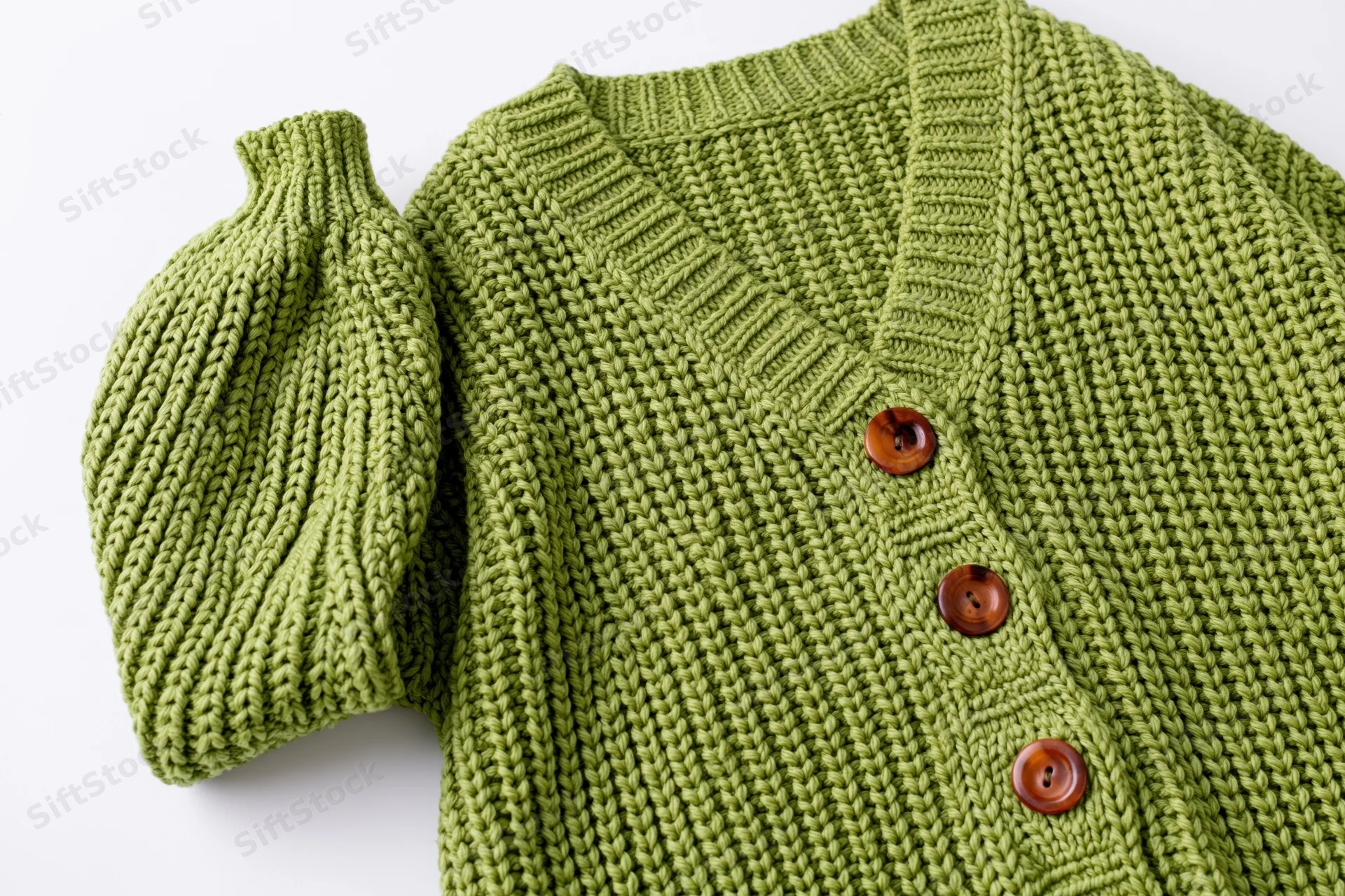 Green knit cardigan laid flat with one sleeve raised on white background