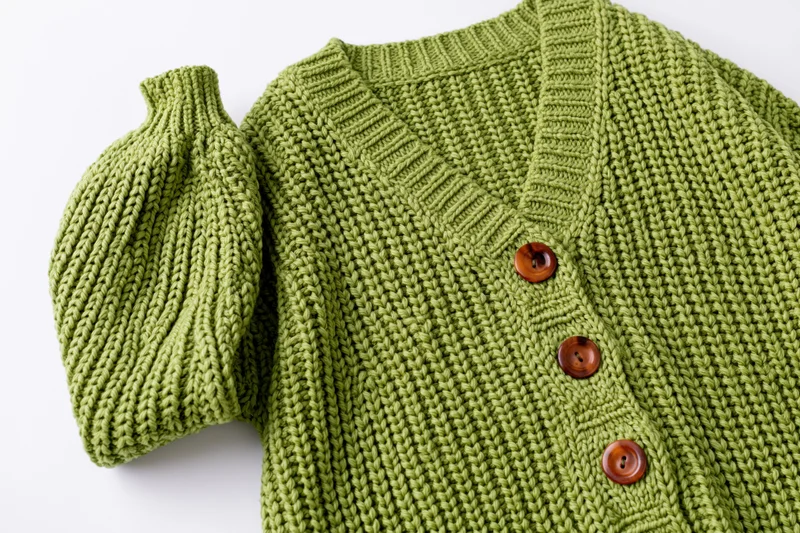 Green knit cardigan laid flat with one sleeve raised on white background