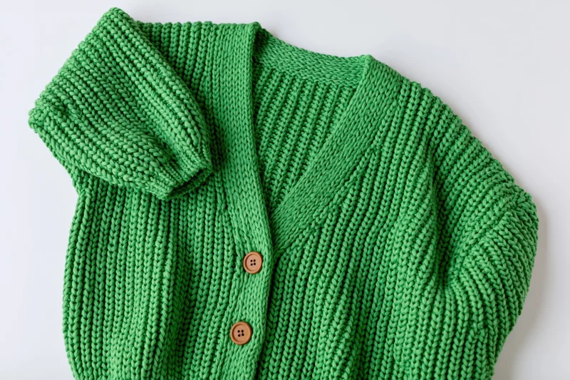Green knit cardigan laid flat with one sleeve raised on white surface