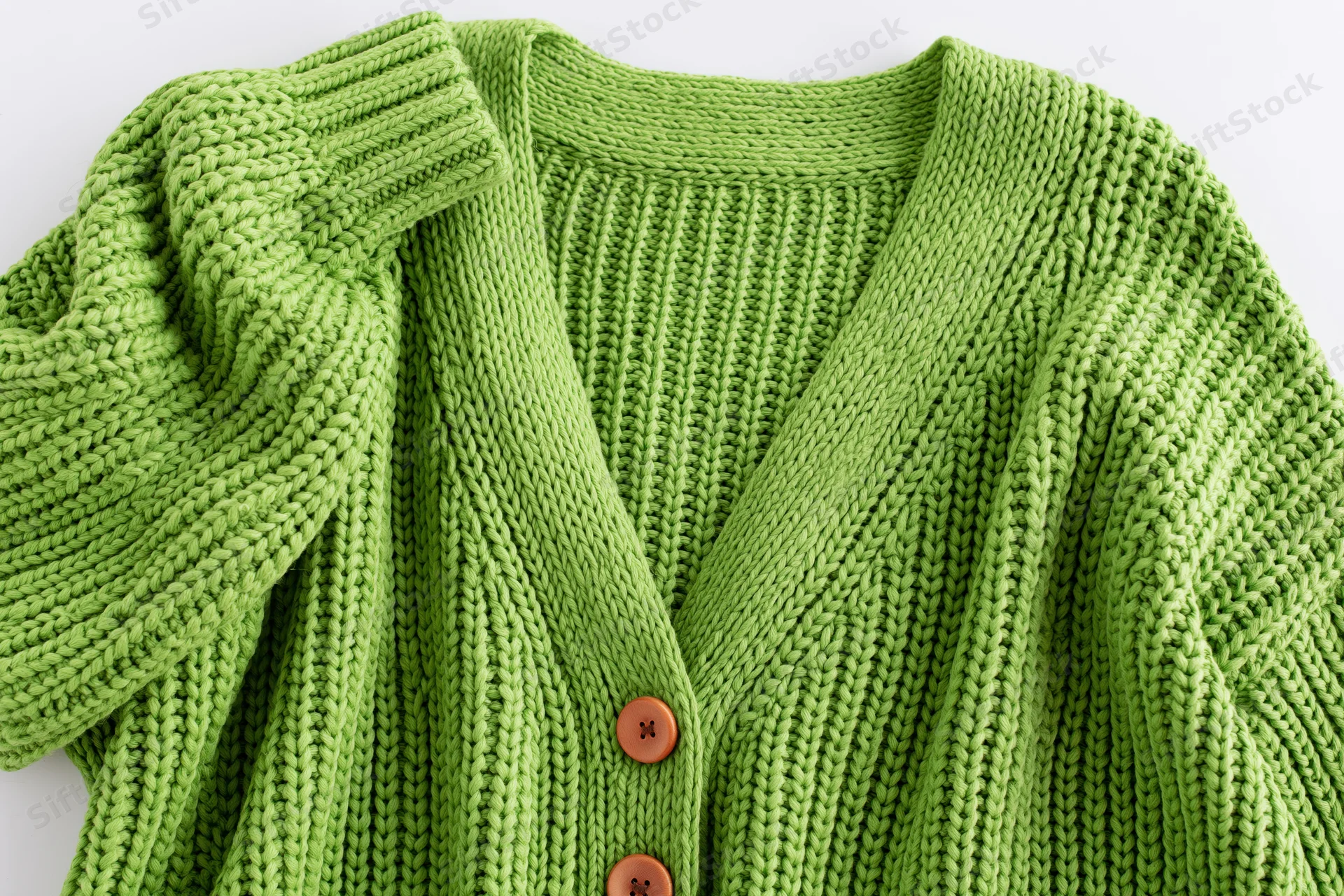 Green knit cardigan laid flat with one sleeve raised on white background
