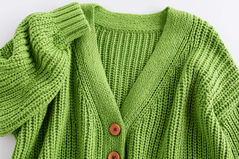 Green knit cardigan laid flat with one sleeve raised on white background