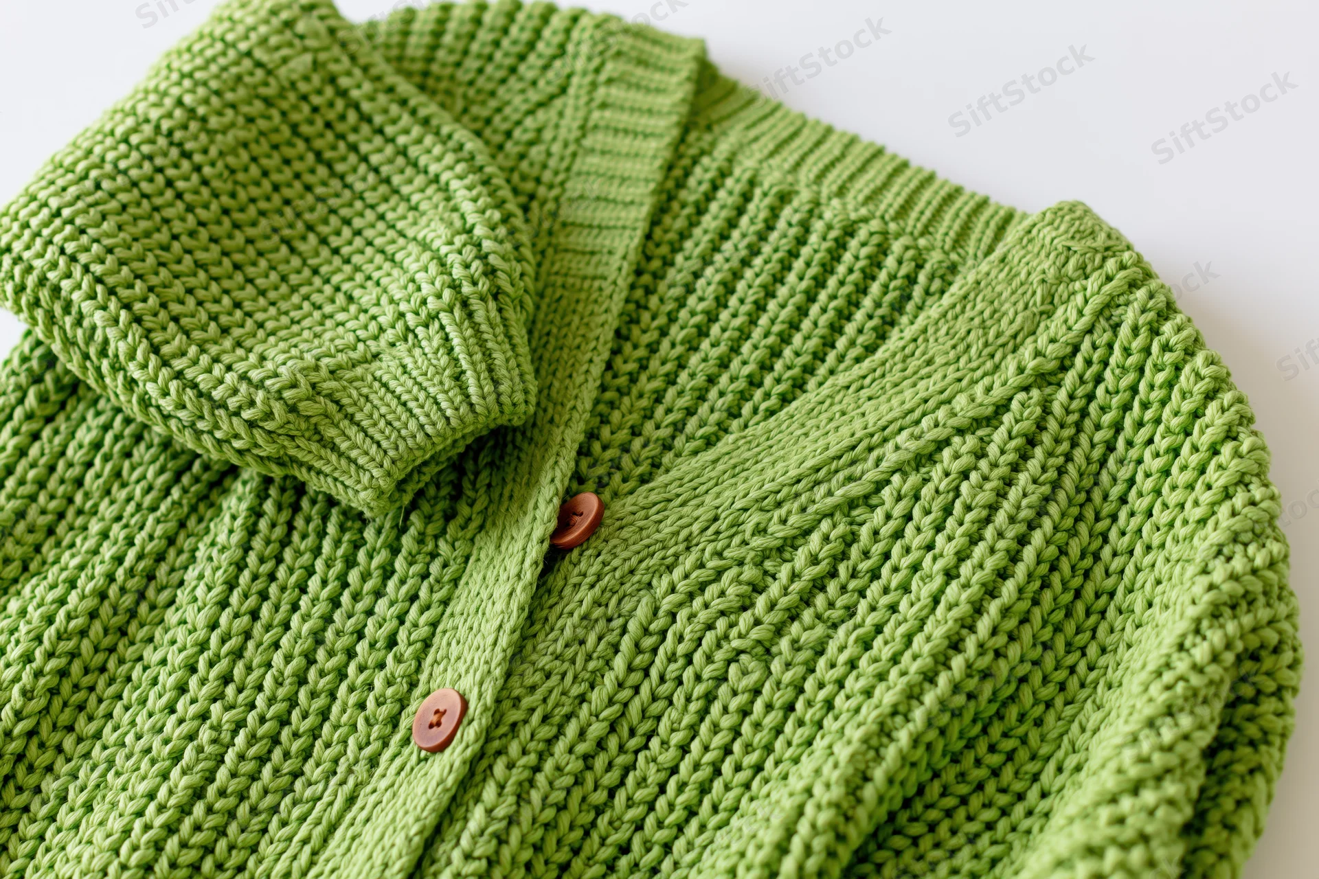 Green knit cardigan with ribbed collar and buttons lying flat, one sleeve raised