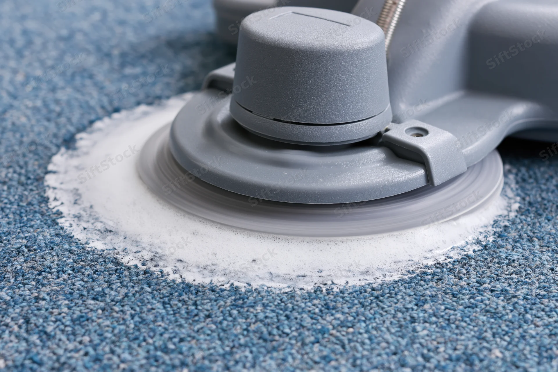 Gray rotary carpet cleaning machine scrubbing blue carpet with foamy detergent