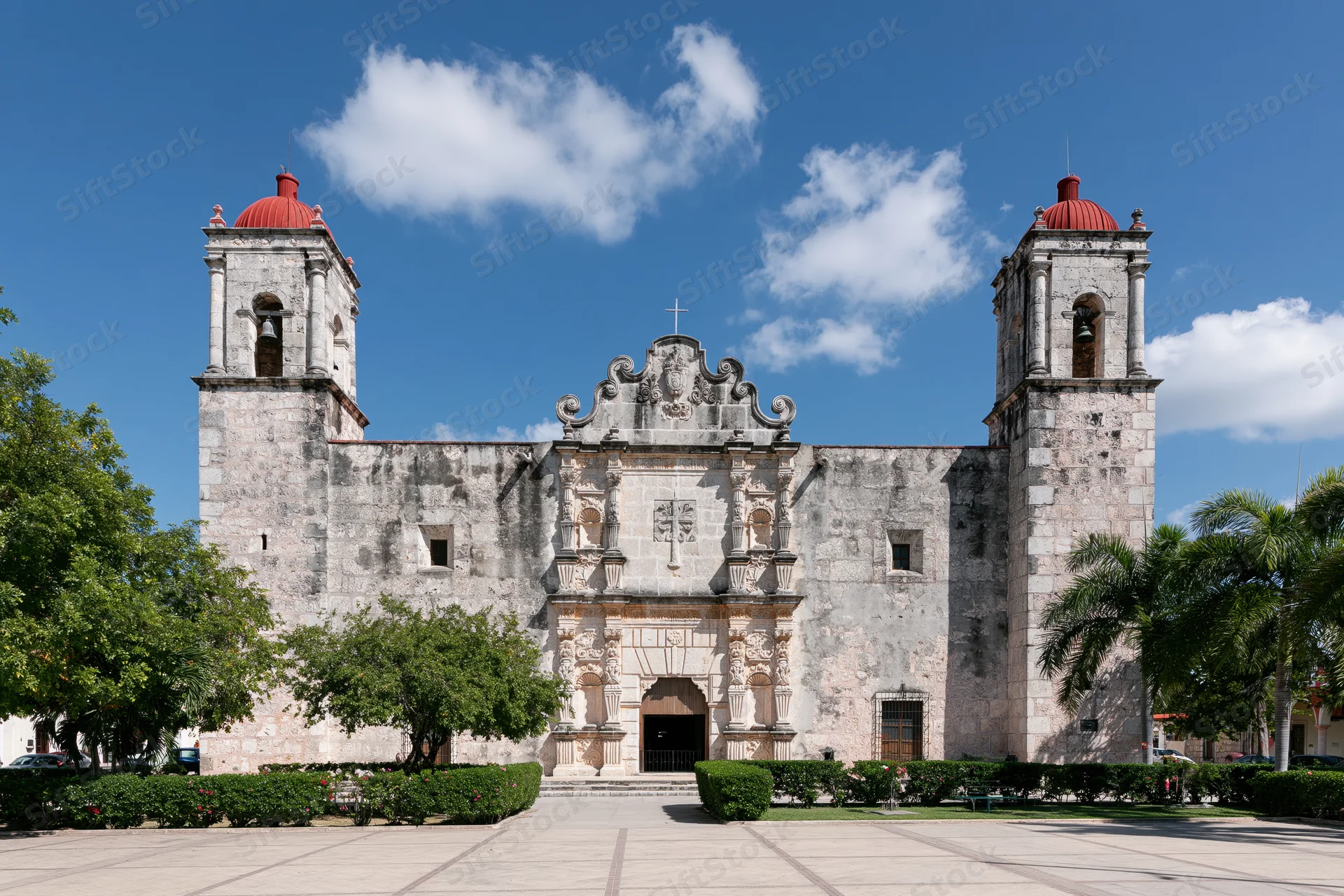 Historic spanish colonial catholic church with twin bell towers and ornate facade in a paved plaza under blue sky