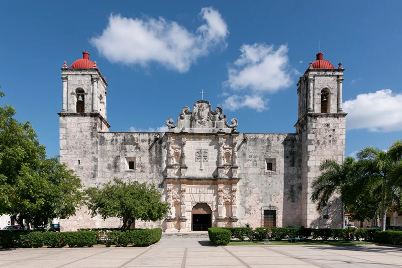 Historic spanish colonial catholic church with twin bell towers and ornate facade in a paved plaza under blue sky