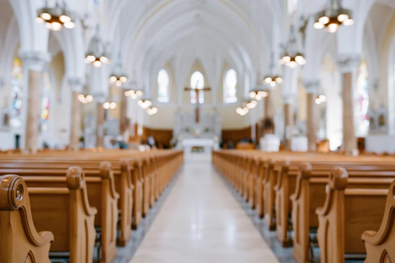 Interior of a catholic church nave with wooden pews lining a central aisle leading to the altar and cross