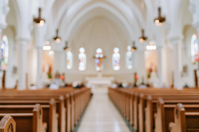 Interior of a catholic church nave with wooden pews and arched ceiling leading to altar