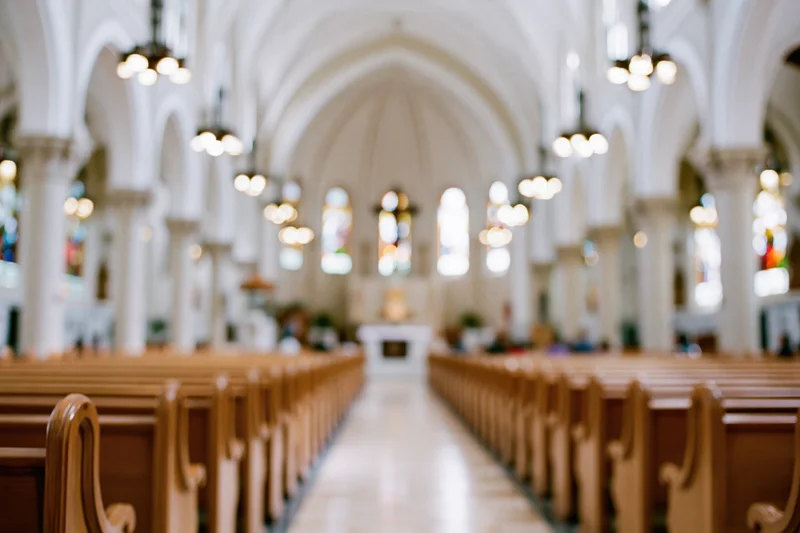 Interior of a catholic church nave with wooden pews and arched ceiling viewed from the back