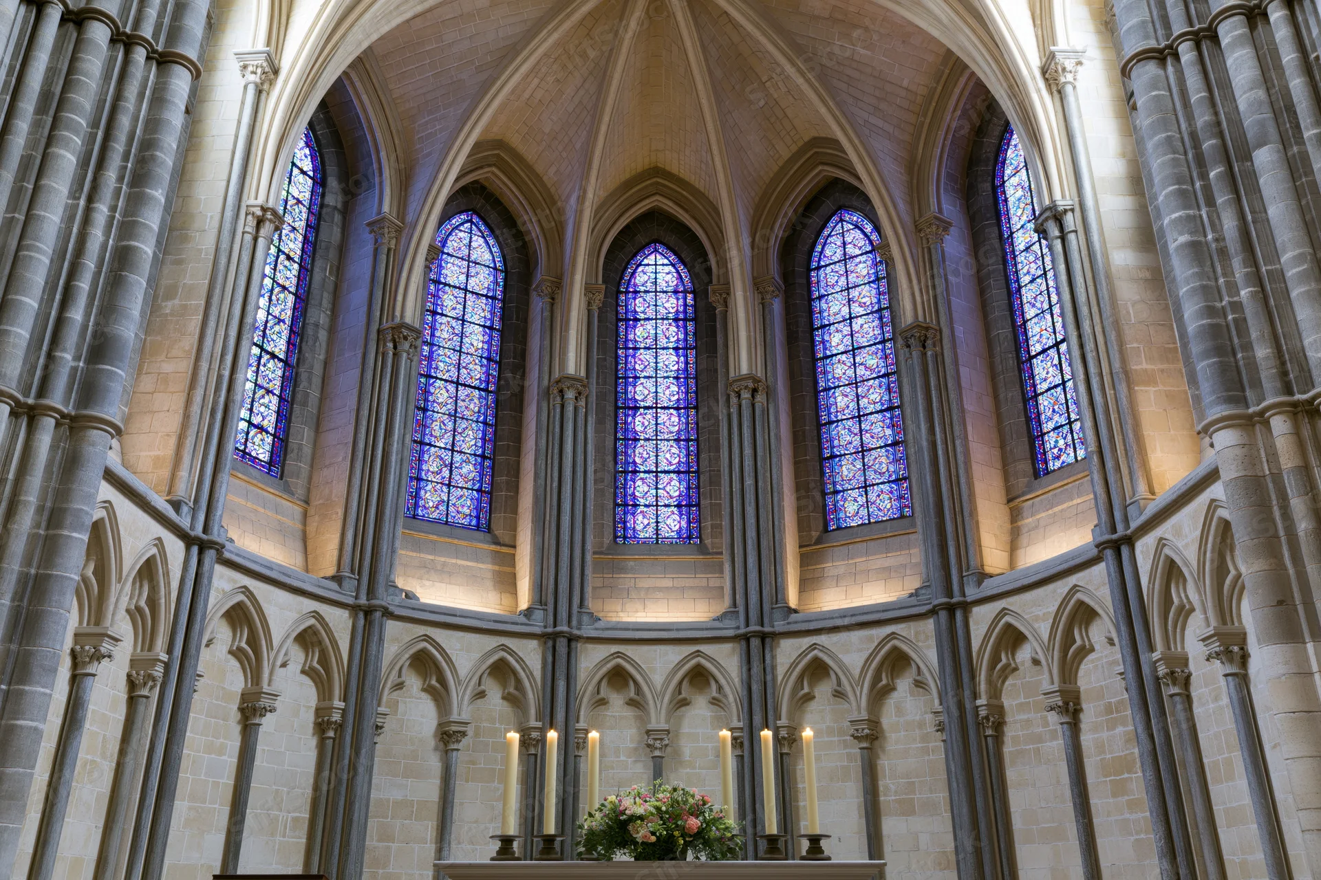Wide symmetrical view of gothic cathedral apse interior with stained glass windows and altar candles