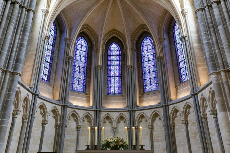 Wide symmetrical view of gothic cathedral apse interior with stained glass windows and altar candles