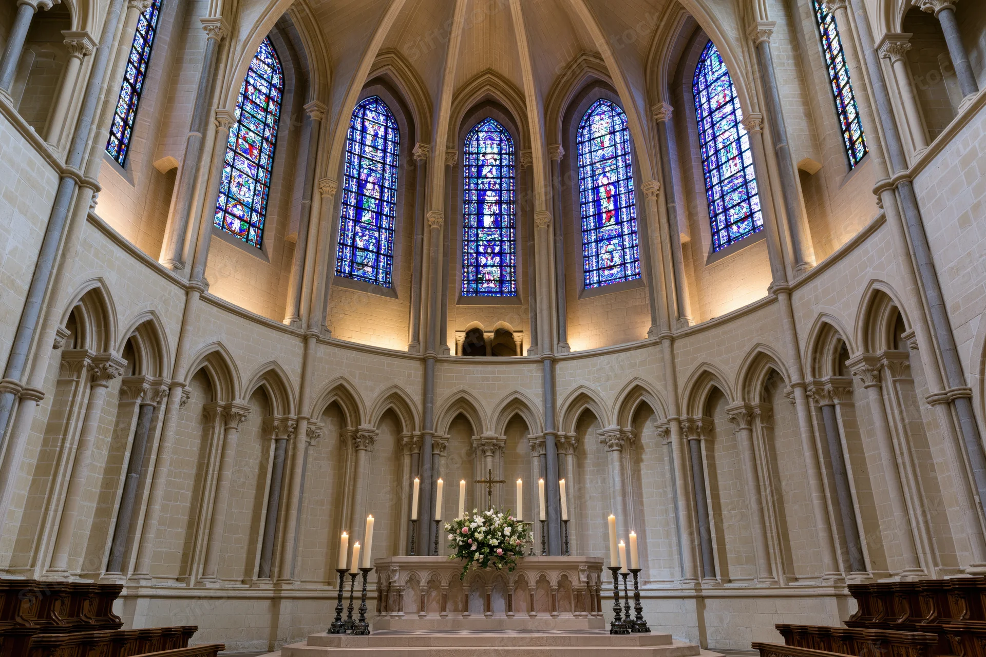 Wide symmetrical view of a gothic cathedral apse interior with stained glass windows and altar