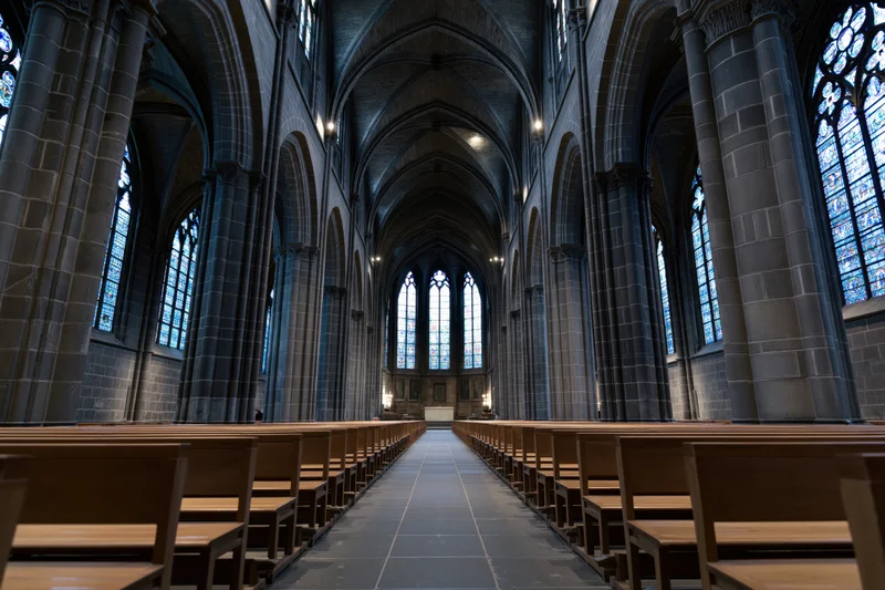 Gothic cathedral nave with wooden pews receding into distance under vaulted stone ceiling